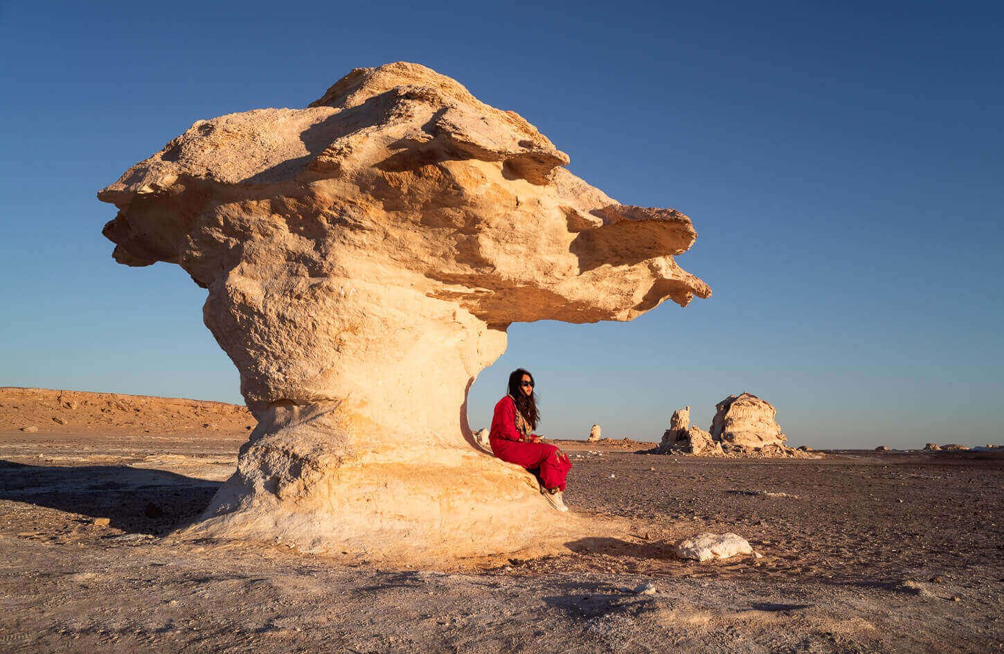 A girl standing on a white dune in the White Desert, surrounded by stunning white sand formations under a clear blue sky.