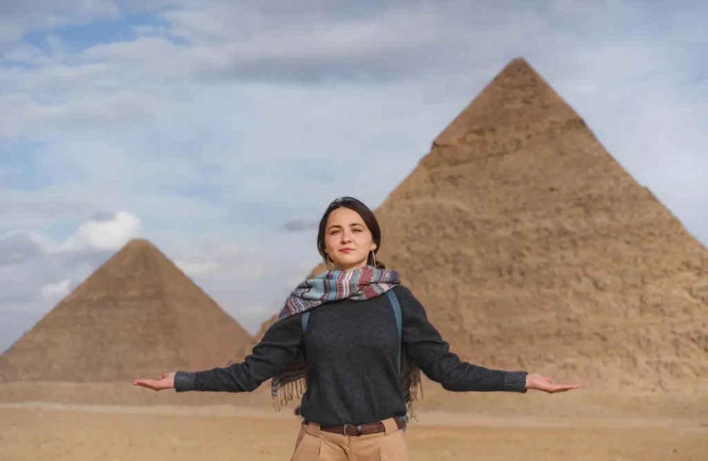 A visitor with arms outstretched in front of the pyramids