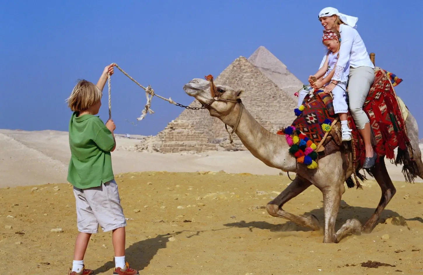 A mother and child on a camel in front of the pyramids