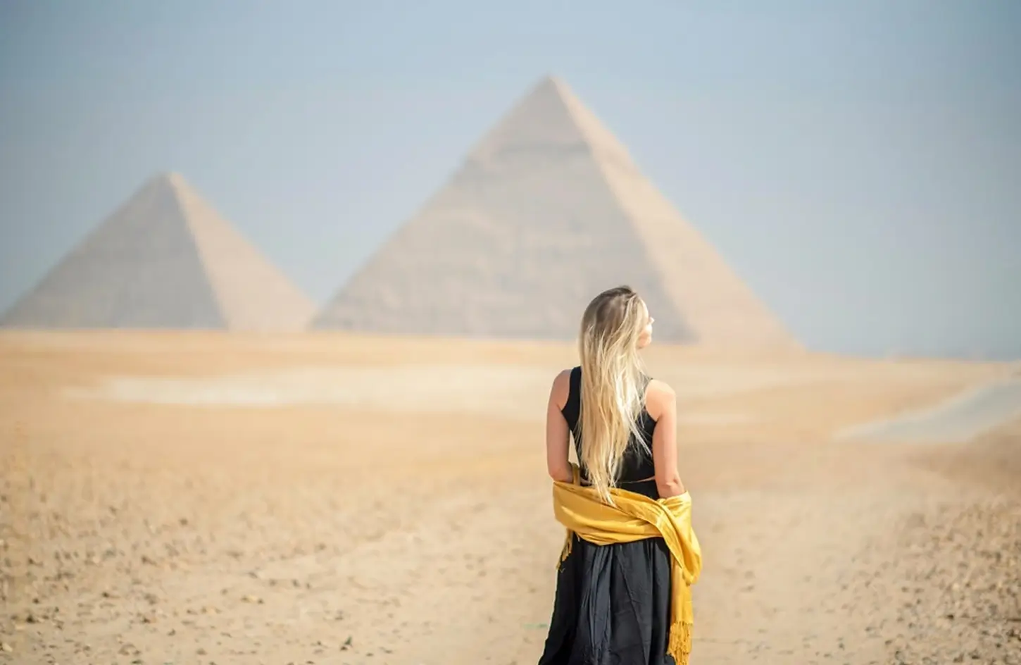 A visitor in a yellow scarf in front of the pyramids
